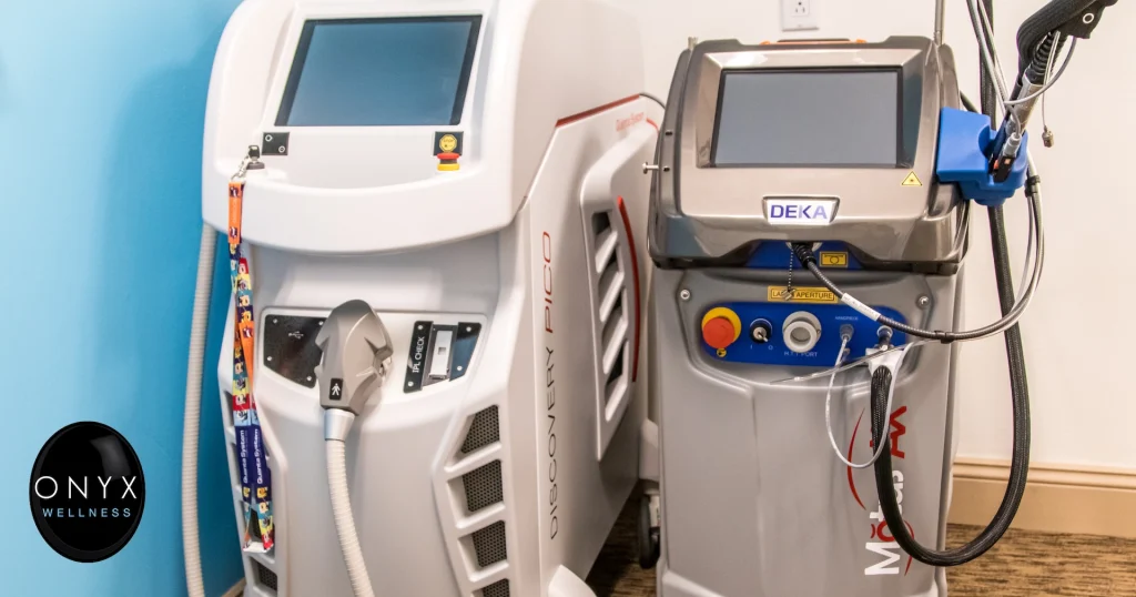 Two professional laser treatment machines side by side in a clinical setting — a Discovery Pico laser device on the left and a DEKA laser system on the right, both with touchscreens and treatment handpieces.