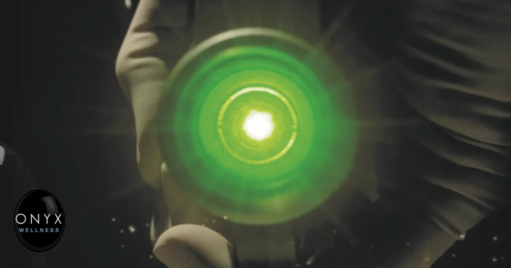 Close-up of a glowing green laser handpiece being held by a gloved hand against a dark background, emitting a bright white light at its center.
