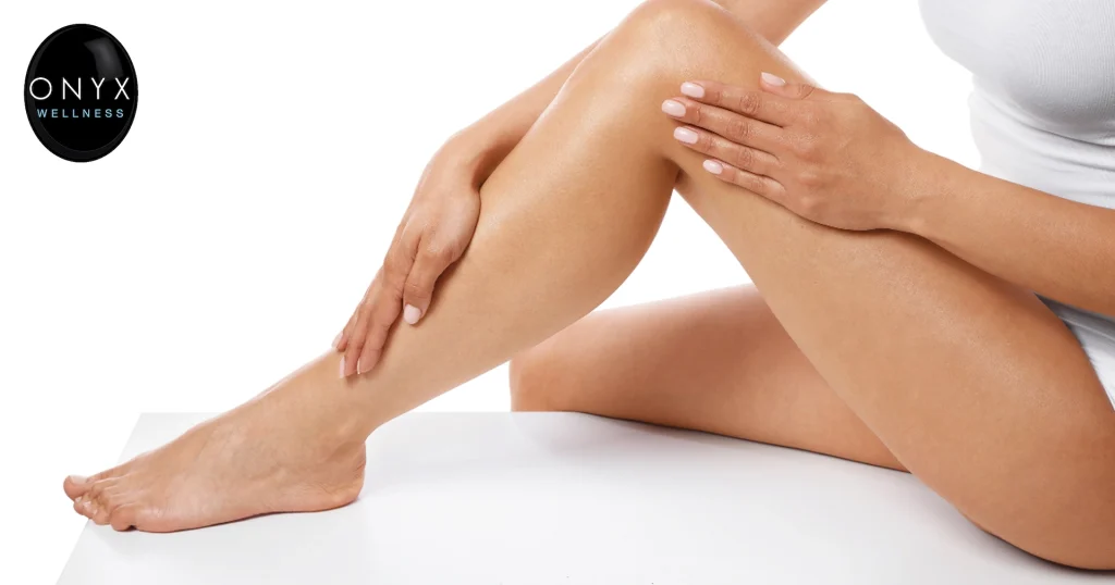 Woman sitting with smooth, hair-free legs while gently touching her skin, representing laser hair removal and aesthetic wellness services.